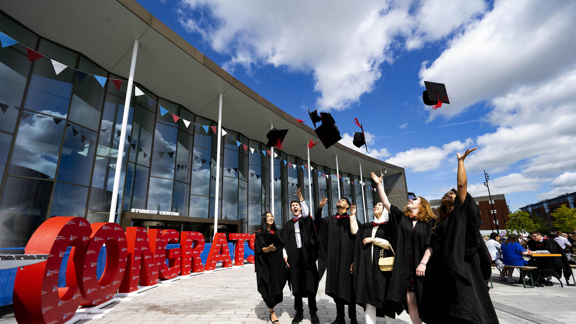 group of graduation students throwing their caps in the air next to a congratulations sign outside the student centre