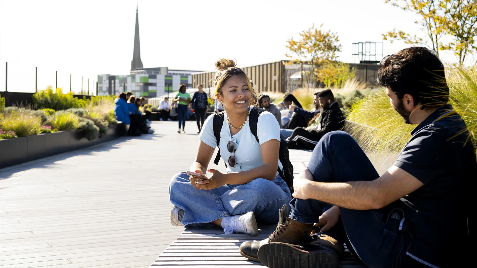 group of students sat in the student centre rooftop garden with a church spire in the background