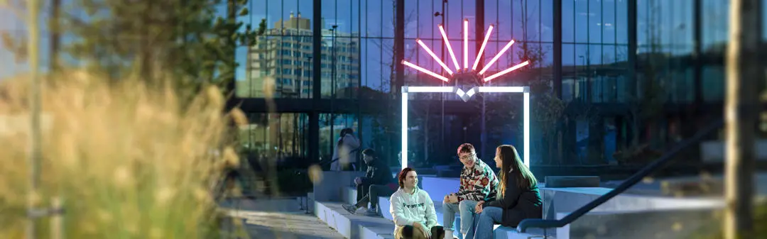 group of students sat on the steps outside the eic, decorative shield in the background